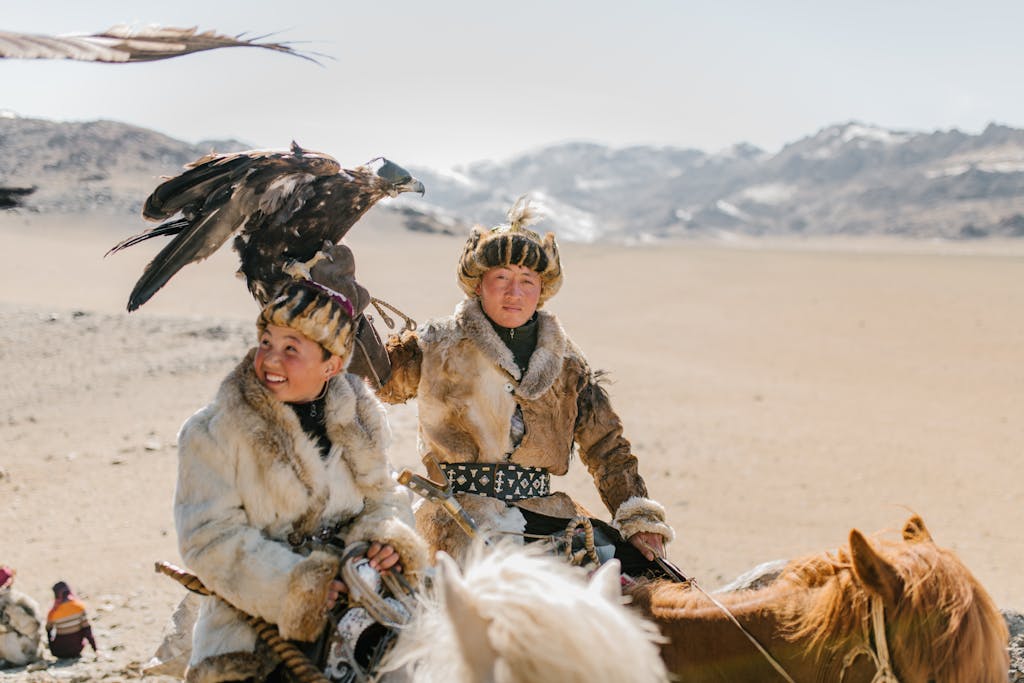 Positive Mongolian eagle hunters riding horses on mountainous terrain