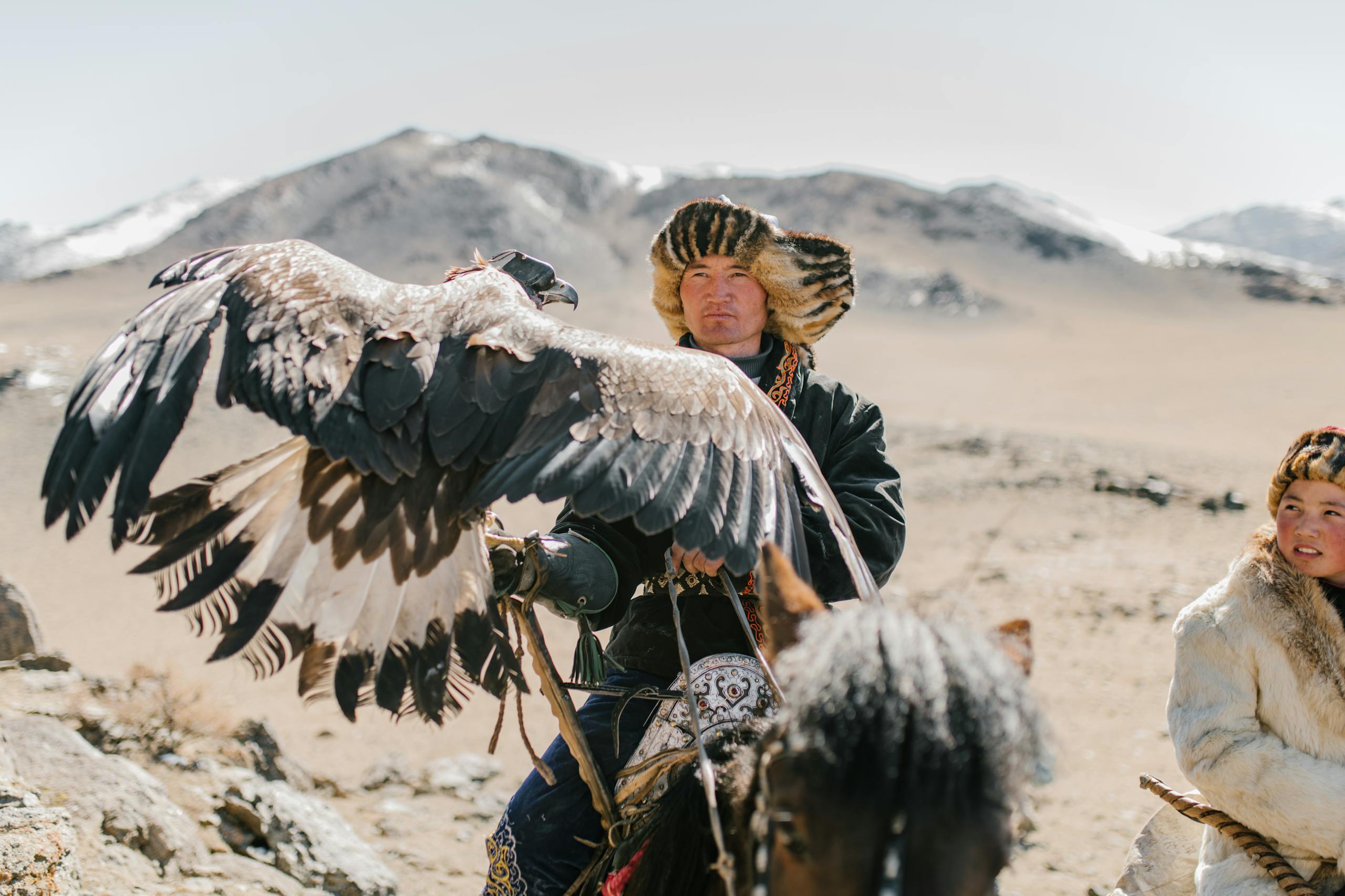 Serious Mongolian hunters with eagles riding horses in highlands