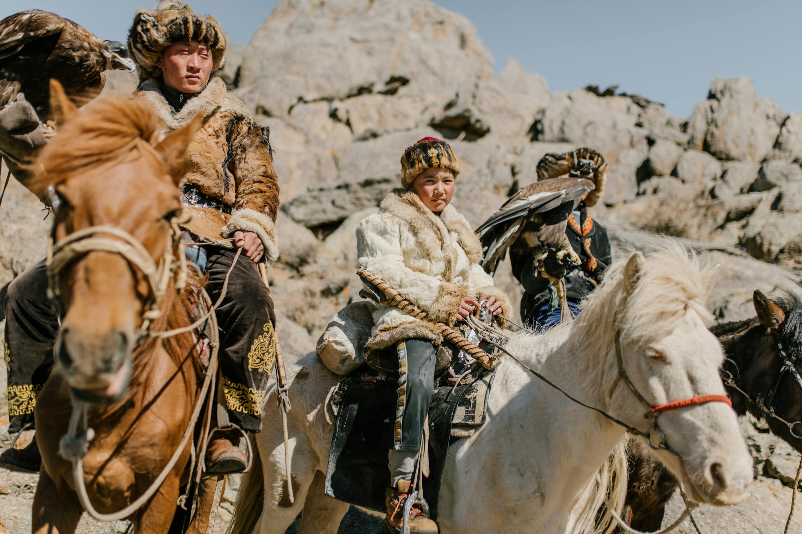 Mongolian eagle hunters in traditional attire with their birds on horseback.